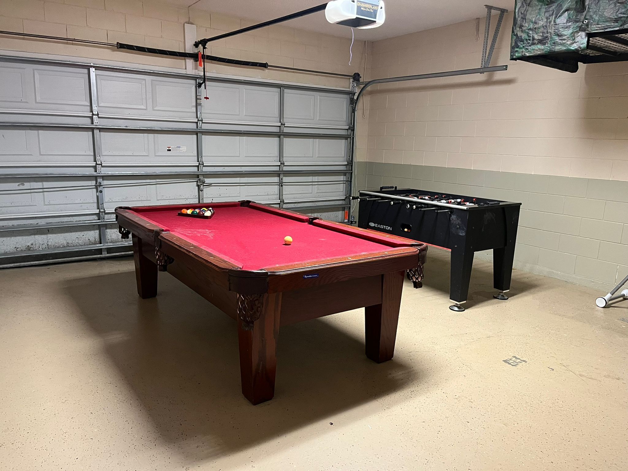 A pool table with balls, a foosball table, and a garage door in the background.
