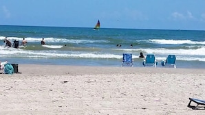 Una playa con varias sillas azules y un velero en el agua.