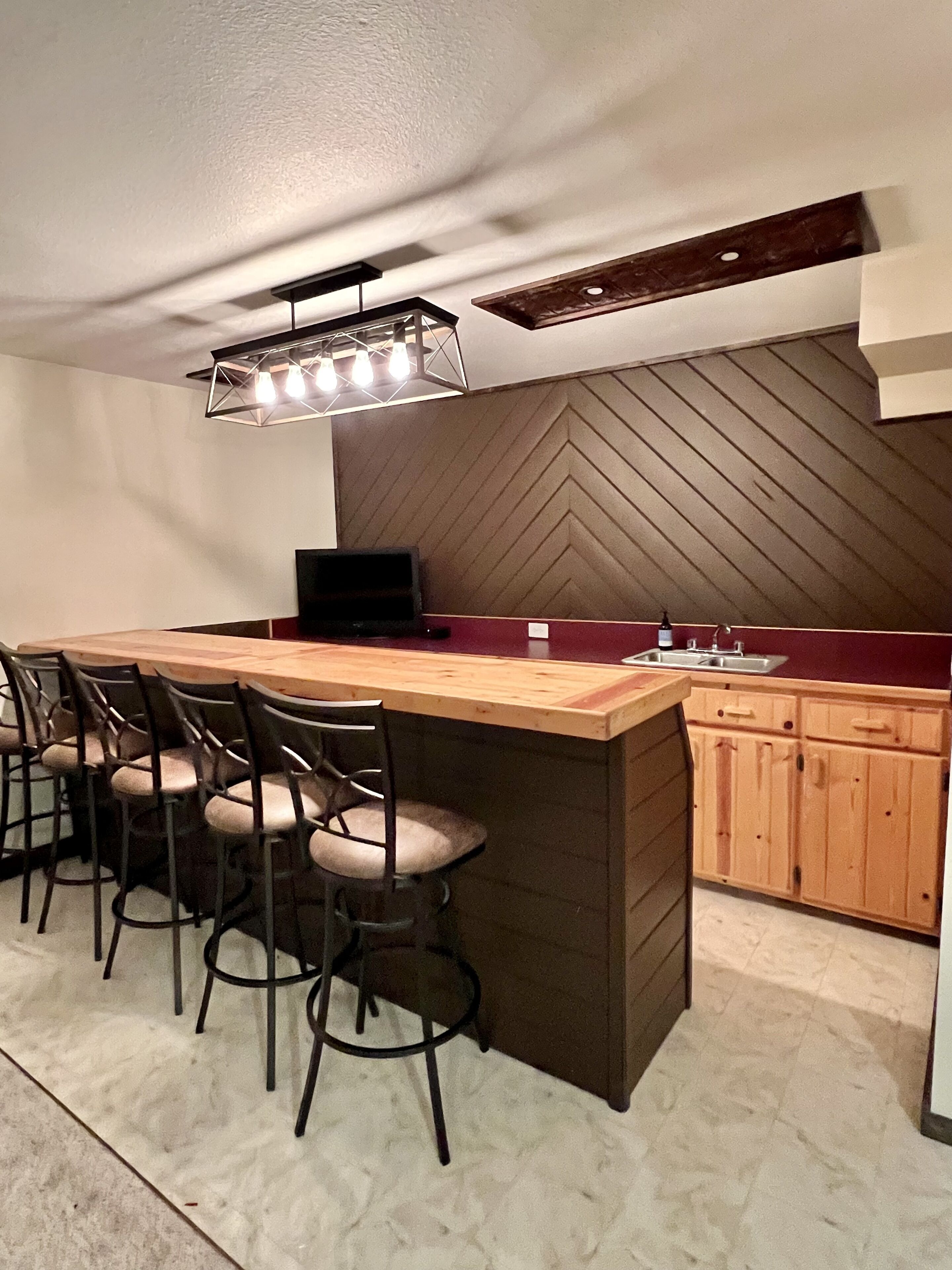 Une cuisine moderne dotée d’un îlot central, de tabourets de bar, d’un évier encastré et d’un mur orné d’un motif en chevrons.