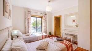 A hotel room with two beds, a desk, a mirror, and a window with curtains. - Modern & Spacious Flat with Pool close to Oura (Albufeira)