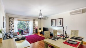 A dining area with a wooden table set for two, a red rug, wicker chairs, and a chandelier. - Modern & Spacious Flat with Pool close to Oura (Albufeira)
