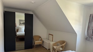 A bedroom with a bed, two wicker chairs, a white wall, and a wooden floor. - Cozy vacation home for 4-6 persons with garden in Trassenheide (Trassenheide)