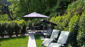 An outdoor patio area with a table and chairs, a covered umbrella, and a pathway. - Vacation apartment Panoramablick (Oberharmersbach)