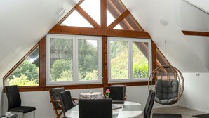 A dining area with a table and chairs, a hanging chair, and large windows with a view of greenery. - Vacation apartment Panoramablick (Oberharmersbach)