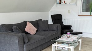 A modern living room with a grey sofa, a black chair, and a glass coffee table. - Vacation apartment Panoramablick (Oberharmersbach)