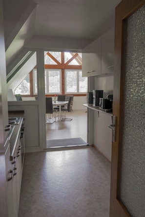 Eine Küche mit Essbereich, einer Treppe und Blick auf Bäume durch große Fenster.