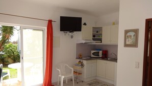A compact living space with a kitchenette, a dining area, and a sliding glass door leading to a patio. - Cozy studio in the garden with terrace (Lagoa / Porches)