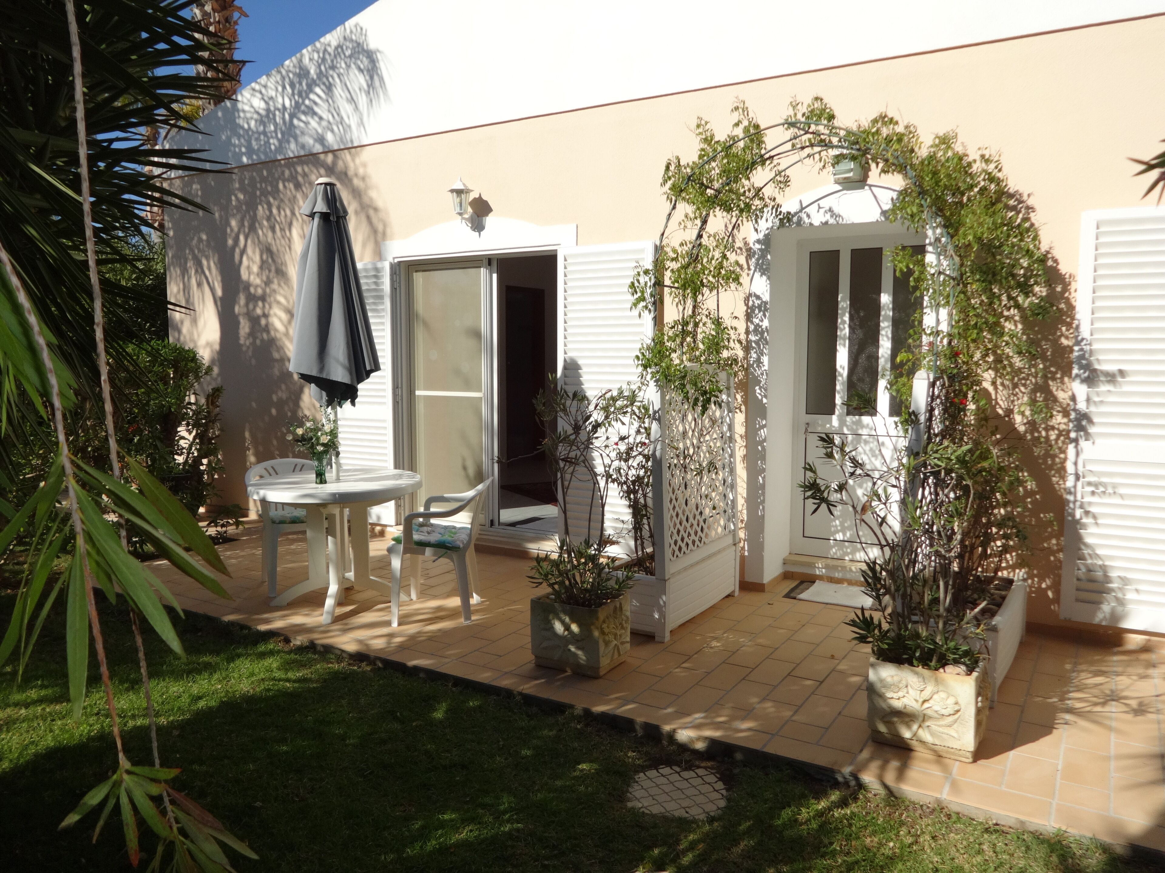 A patio with a table and chairs, a door, and potted plants.