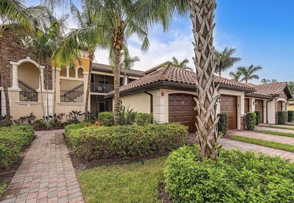 A residential building with a brick pathway, palm trees, and a well-maintained garden.