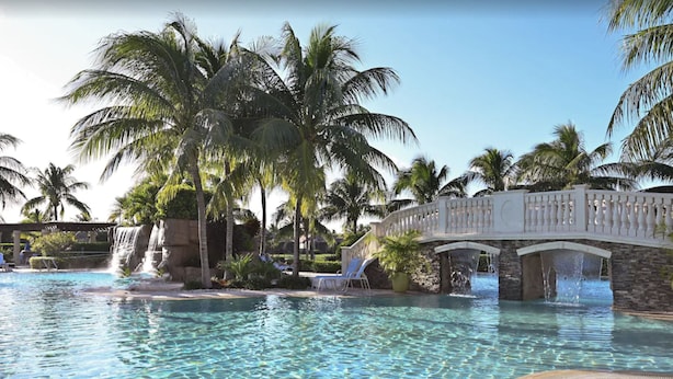 Una piscina cristalina con un puente, palmeras y sillas de descanso.