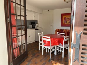 Une cuisine compacte avec des meubles blancs, un four à micro-ondes et une machine à café. Un coin repas est aménagé avec une table rouge et des chaises blanches.