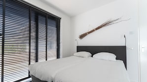 Un dormitorio moderno con una cama grande, cabecera negra y ropa de cama blanca.