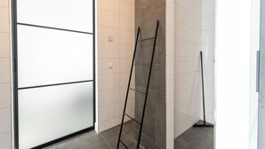 Un pasillo con una puerta corredera, una escalera apoyada en la pared y un trapeador apoyado en la pared.