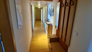 Un couloir étroit avec un plancher en bois, un banc et un porte-manteau.