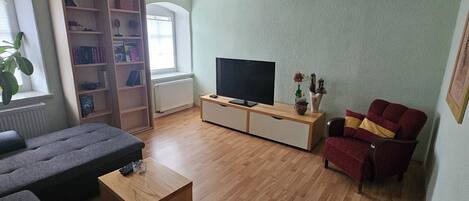 A living room with a sofa, a coffee table, a TV on a wooden stand, a bookshelf, and a red armchair.