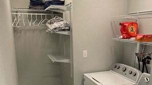 Een wasserette met een wasmachine, een droger, een plank met Tide wasmiddel en een ophangrek met opgevouwen kleding.