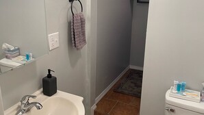 Een badkamer met een wit wastafelmeubel, een spiegel, een handdoekhouder, een toilet en een klein plankje met toiletartikelen.