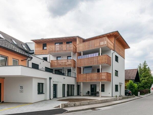 Un immeuble moderne à plusieurs étages, doté de balcons en bois, d’un toit plat et d’un espace de stationnement.