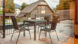A terrace with a table and chairs, a wooden building in the background, and a view of a village. - Apartment Near ski Area in Groebming (Groebming)