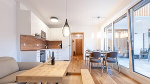 A modern kitchen with white cabinets, a wooden countertop, and a dining area with a wooden table and chairs. - Apartment Near ski Area in Groebming (Groebming)