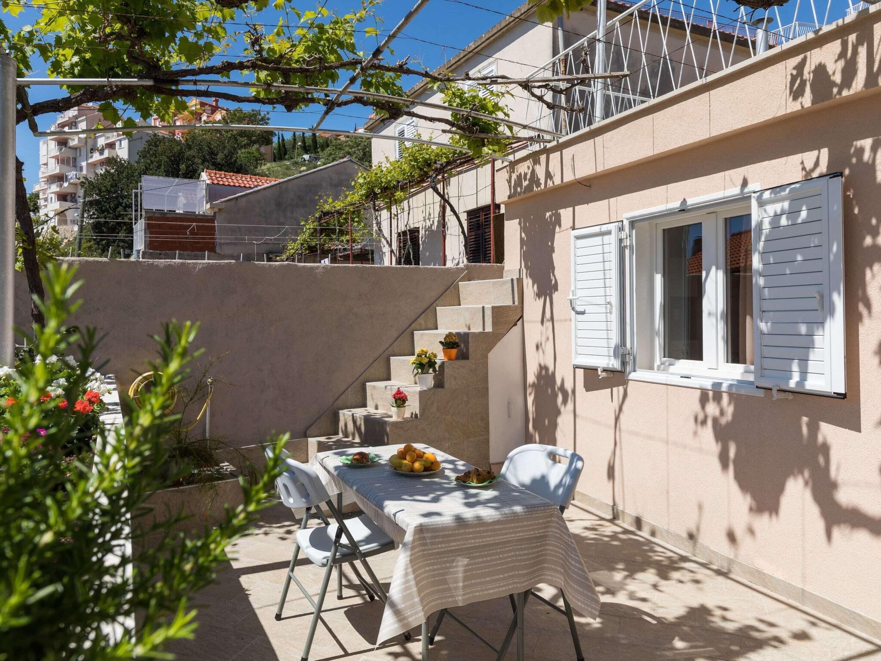 Un patio al aire libre con una mesa lista para dos personas, rodeado por un muro bajo y una escalera que lleva a un balcón.