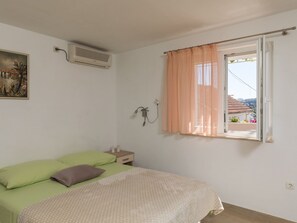 Une chambre à coucher comprenant un lit, une table de chevet, une fenêtre avec des rideaux, un appareil de climatisation et un luminaire fixé au mur.