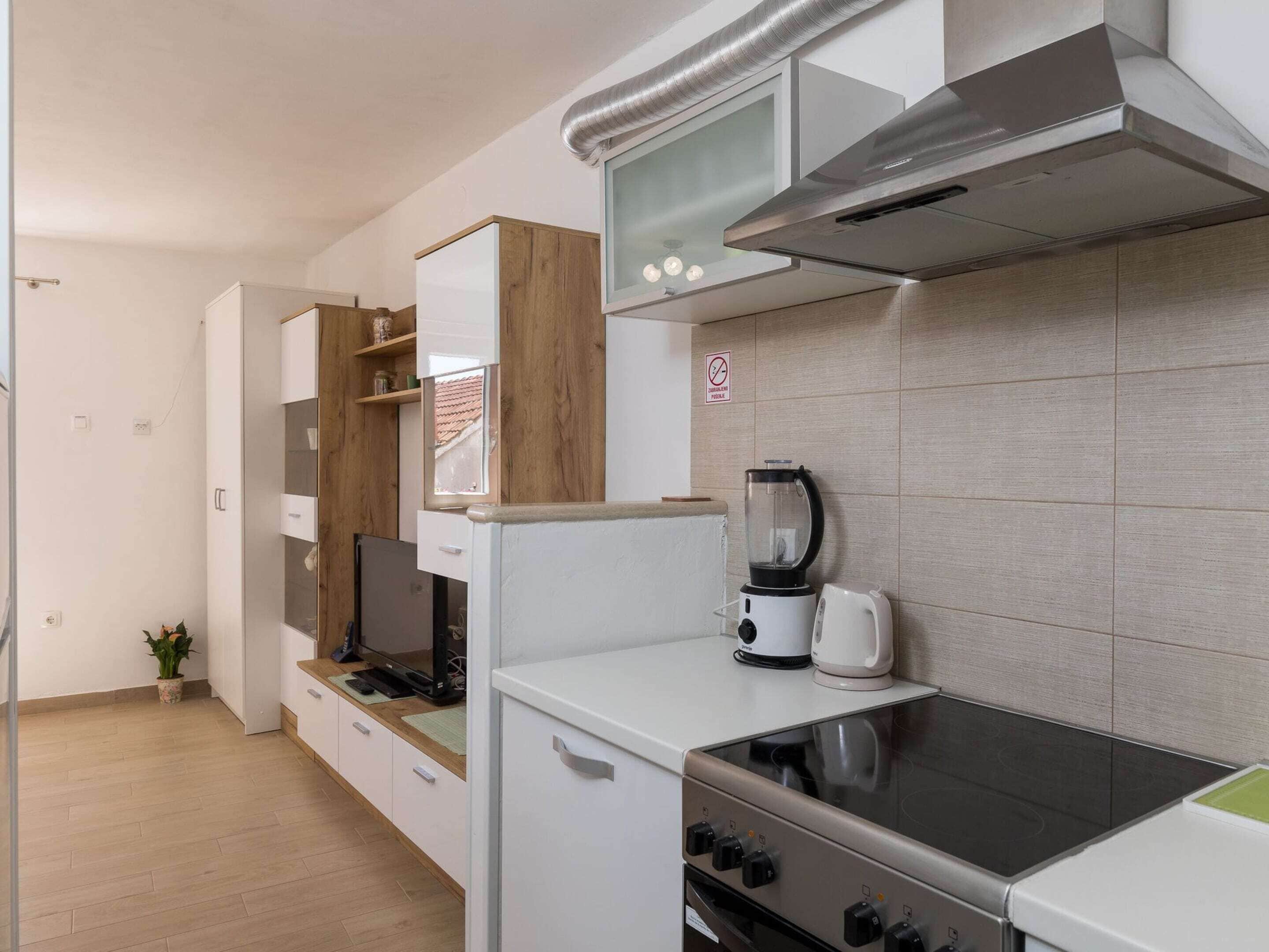 A modern kitchen with white cabinets, a built-in oven, a stove, a coffee maker, and a blender.