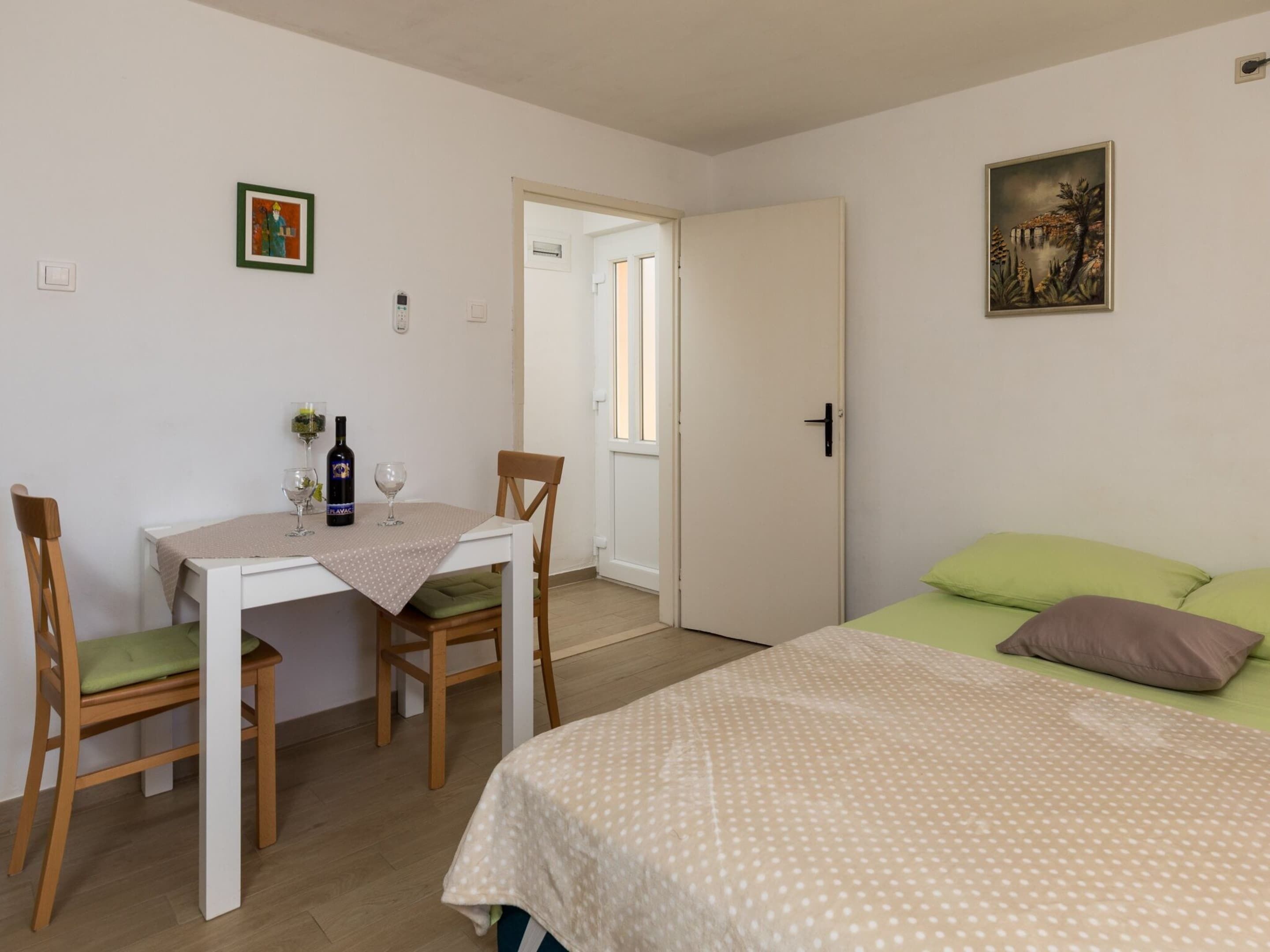 A room with a bed, a table with chairs, a bottle of wine, and a painting on the wall.