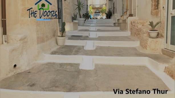 Una calle estrecha con escalones que conducen a un edificio. El edificio tiene un letrero que dice "The Doors". Hay plantas en macetas en los escalones y a lo largo de los lados de la calle.