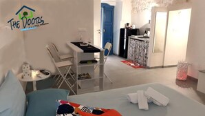 Habitación de hotel con cama, un pequeño escritorio con silla, zona de comedor con mesa y sillas, y cocina con refrigerador y fregadero.