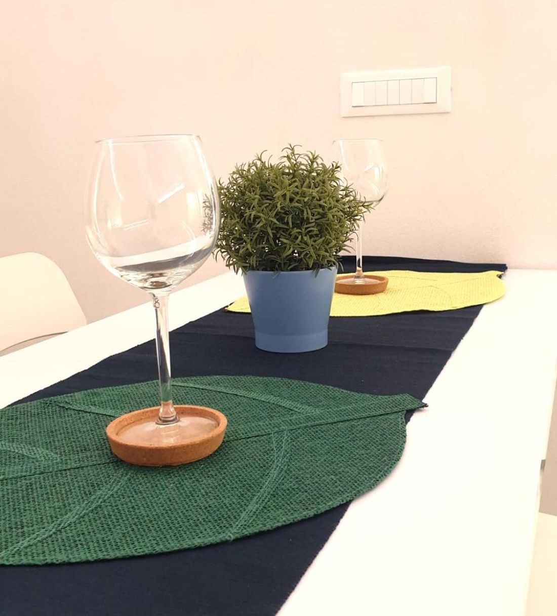 Una habitación con una cama, una planta en maceta y dos copas de vino sobre un tapete.