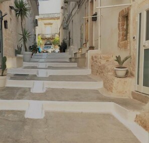 Una calle estrecha con escalones que conducen a un edificio. El edificio tiene un letrero que dice "The Doors". Hay plantas en macetas en los escalones y a lo largo de los lados de la calle.