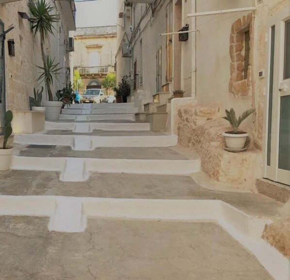 Une rue étroite avec des marches menant à un immeuble. L’immeuble porte une enseigne sur laquelle on peut lire « The Doors ». Des plantes en pot sont disposées sur les marches et le long des côtés de la rue.
