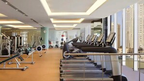 Un gimnasio con cintas de correr, máquinas de pesas y vistas a la ciudad.