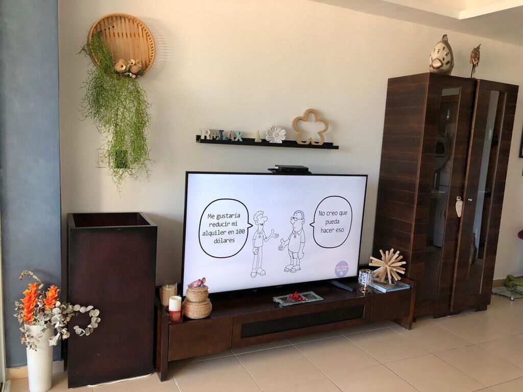 Un salon avec un téléviseur à écran plat posé sur un meuble en bois, un buffet sombre et une étagère décorative où sont exposés divers objets.