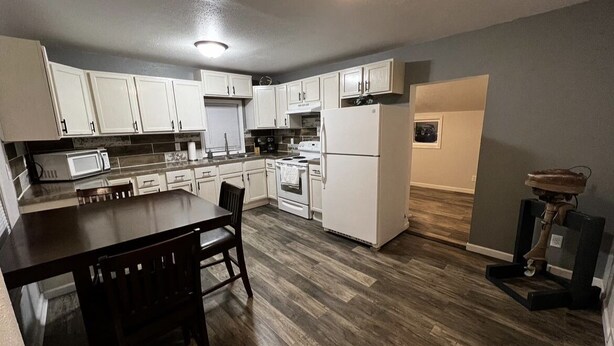 Una cocina con armarios blancos, una mesa de comedor de madera y un refrigerador.