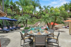 A poolside area with lounge chairs, a dining table set for six, and a small waterfall feature. - Villa Paradiso (El Cajon)