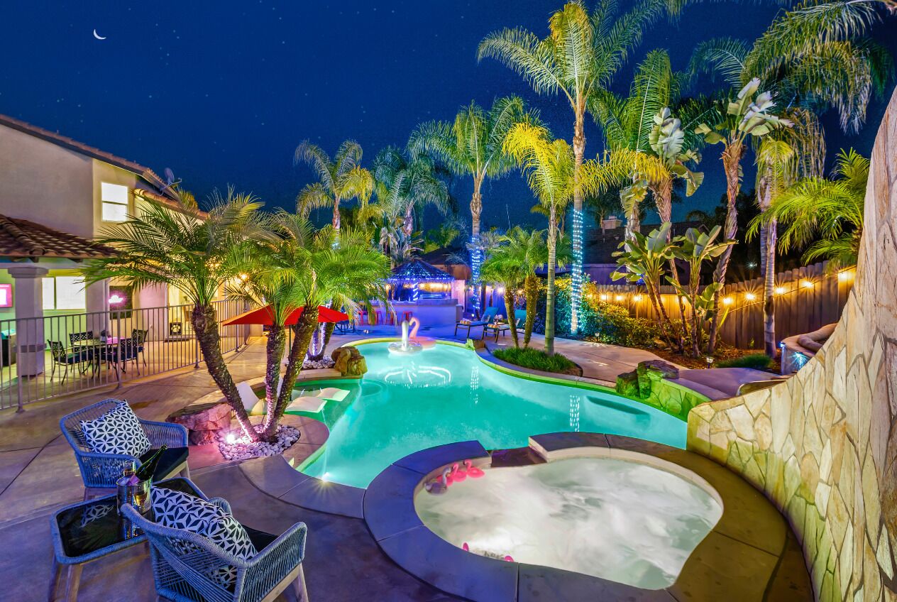 A nighttime outdoor pool area with lounge chairs, a hot tub, and palm trees.
