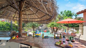An outdoor pool area with a thatched roof, lounge chairs, and a buffet table with food and drinks. - Villa Paradiso (El Cajon)