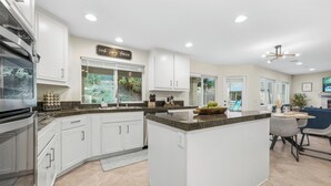 A modern kitchen with white cabinetry, granite countertops, and a central island. - Villa Paradiso (El Cajon)