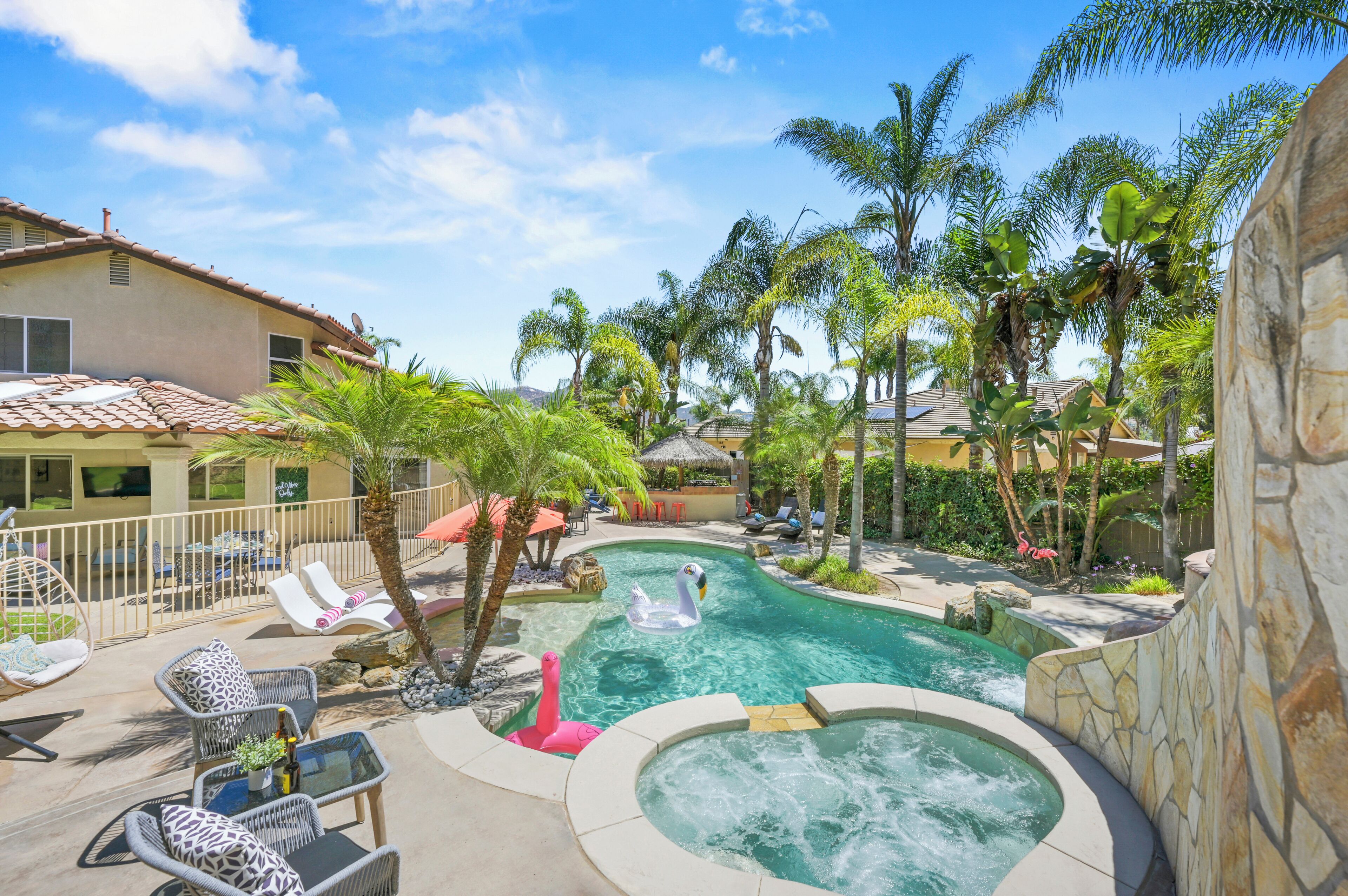 A pool area with lounge chairs, a hot tub, and palm trees.