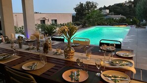 Mesa de comedor lista para una comida, con vista a una piscina y el paisaje circundante.