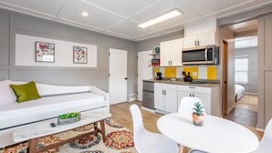 Una cocina moderna con armarios blancos, un microondas y una cafetera. Hay un comedor con mesa y sillas blancas, y un sofá con un cojín verde.