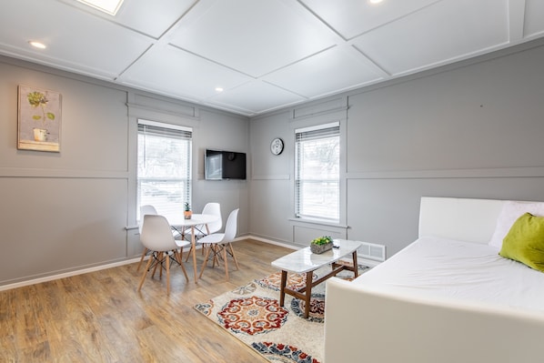 A modern room with a bed, a dining table with chairs, a TV, and a clock on the wall.