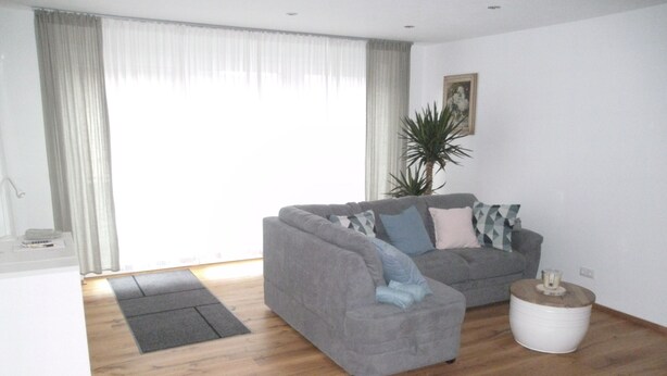 A modern living room with a grey sofa, a small white side table, and a wooden floor. - Double time-out on one floor. Time-out 1 and time-out 2 together (Rattelsdorf)