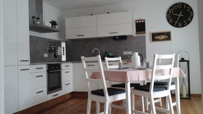 Una cocina moderna con armarios blancos, una mesa de comedor con sillas, un reloj y un adorno en la pared.
