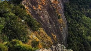A large rock formation with a prominent peak, surrounded by lush greenery and a vast landscape in the background. - POUSADA SERRANO (São Bento do Sapucaí)