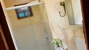 A bathroom with a glass shower enclosure, a toilet, a sink, and a mirror. - POUSADA SERRANO (São Bento do Sapucaí)