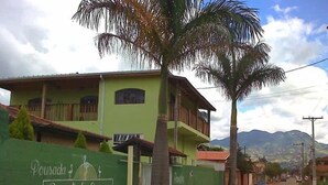 A two-story building with a green facade, a balcony, and a palm tree in front. - POUSADA SERRANO (São Bento do Sapucaí)