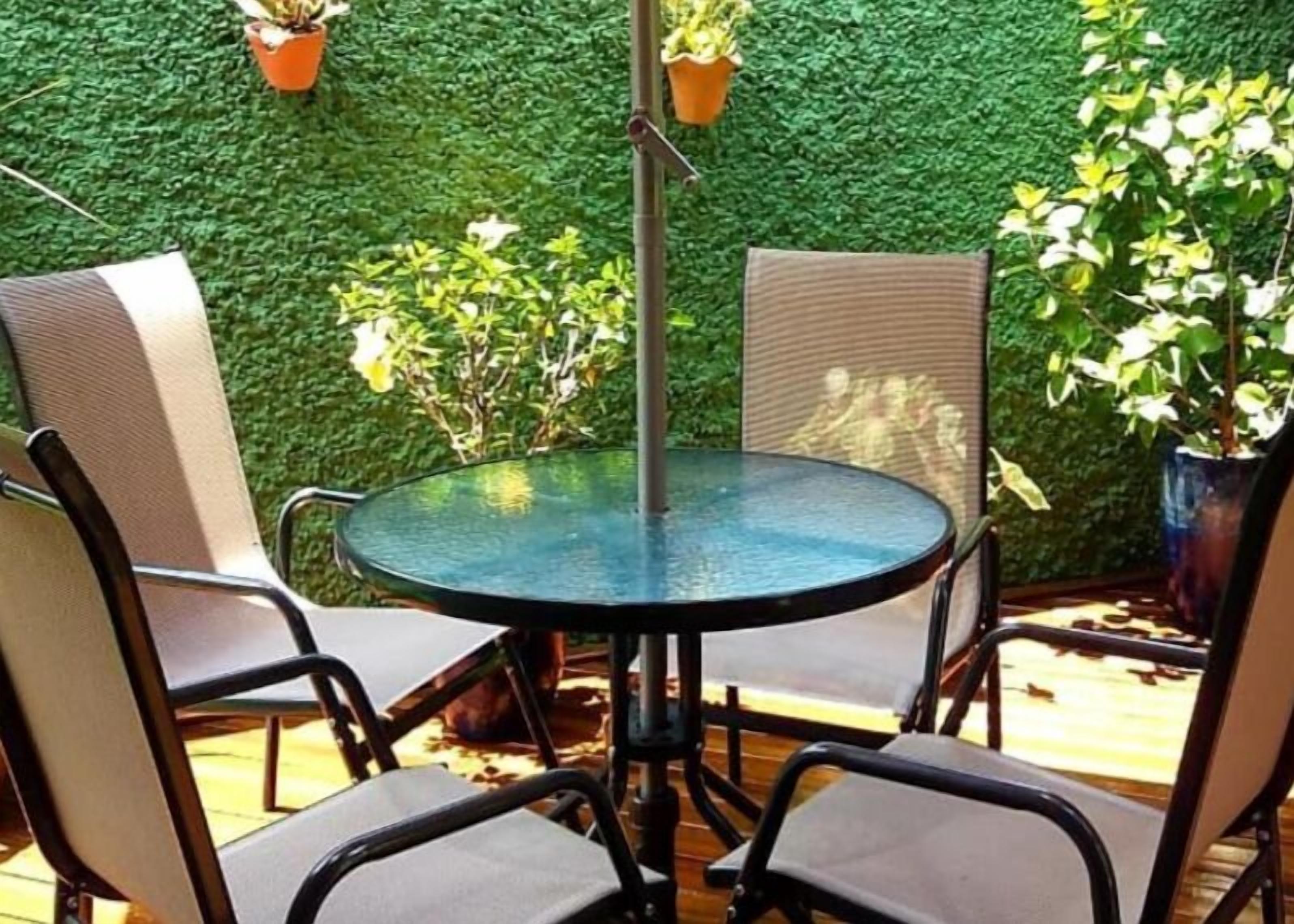 Mesa redonda con cuatro sillas en un espacio exterior con pared verde y plantas en macetas.